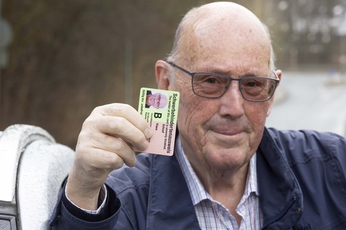 Ein &auml;lterer Mann h&auml;lt seinen Schwerbehindertenausweis mit dem Merkzeichen B hoch. 