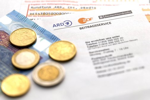 Ein Schreiben des Rundfunkgeb&uuml;hren-Beitragsservice, darauf liegen M&uuml;nzen und ein 20-Euro-Schein, darunter ein &Uuml;berweisungstr&auml;ger