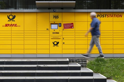 DHL-Poststation Eine Poststation von DHL. Ein Mann geht gerade daran vorbei. Im Vordergrund sieht man eine Treppe.
