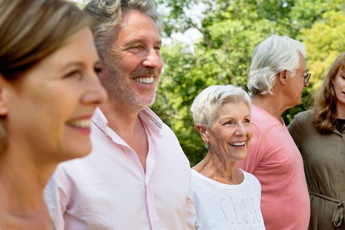 Mehrere M&auml;nner und Frauen sind gut gelaunt, lachen. Sie sind drau&szlig;en im Gr&uuml;nen. 