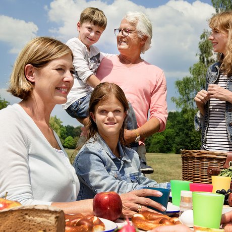 Unterschiedliche Menschen - alt und jung, Männer und Frauen, mit und ohne Behinderung - sitzen draußen auf Bierbänken an einem Tisch, essen gemeinsam.