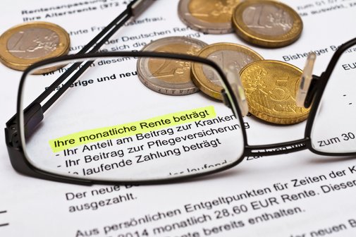 Nahaufnahme eines Rentenbescheids mit markiertem Text &sbquo;Ihre monatliche Rente betr&auml;gt&lsquo;, umgeben von Euro-M&uuml;nzen und einer Brille im Vordergrund.
