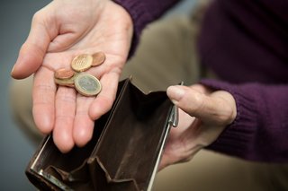 Hände einer Frau halten eine Geldbörse auf, auf der Handfläche der einen Hand liegen wenige Münzen. 