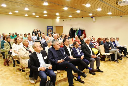 Publikum sitzt in einem Veranstaltungsraum und h&ouml;rt einem Vortrag zu