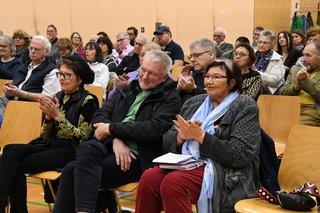 Zuhörende auf Stühlen applaudieren. 