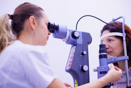 Ärztin schaut durch ein Okular in das Auge ihrer Patientin und justiert gerade an einer Schraube die optimale Einstellung des Apparates. 