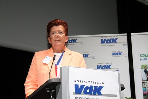 Frau in abrikotfarbenem Blazer am Rednerpult 