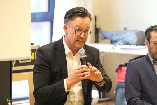 Mann sitzt und spricht in ein Mikrofon w&auml;hrend einer Diskussion