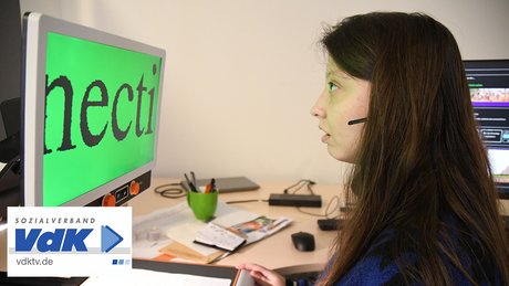 Eine Frau mit Sehbeinderung schaut auf einen Monitor mit stark vergrößerter Schrift.
