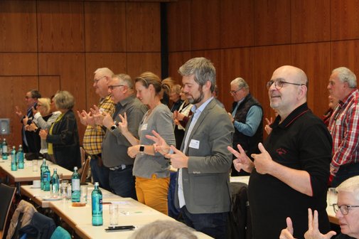 Ganze Reihe von Menschen ist aufgestanden und versucht, ihre Finger in einer bestimmten Abfolge zu krümmen und zu strecken. 