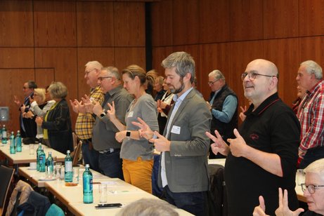 Ganze Reihe von Menschen ist aufgestanden und versucht, ihre Finger in einer bestimmten Abfolge zu krümmen und zu strecken. 