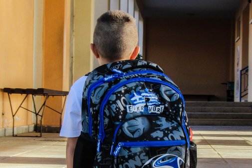 Ein Kind mit Schulranzen auf dem Weg zur Schule von hinten aufgenommen
