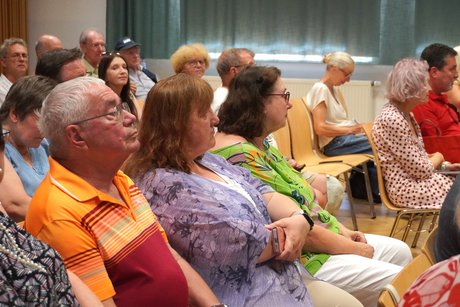 Voller Saal mit vielen &auml;lteren Menschen in bunter Sommerkleidung. 