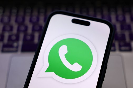Nahaufnahme eines Smartphones mit geöffnetem WhatsApp-Logo auf dem Bildschirm. Im Hintergrund ist unscharf eine Laptop-Tastatur zu sehen.
