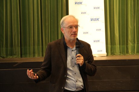 Mann in offenem dunkelbraunen Sakko erklärt etwas