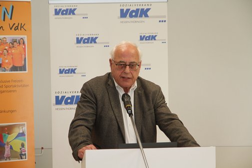 Ein &auml;lterer Mann mit Brille in braunem Jacket an einem Rednerpult