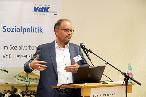 Ein Mann steht an einem Rednerpult und spricht mit Gesten in ein Mikrofon