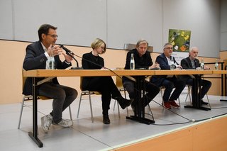 4 Männer und eine Frau sitzen an einem langen Tisch auf dem Podium 