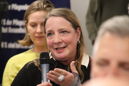Frau aus dem Publikum erklärt, auch mit in die Kamera deutender Geste, die Funktion eines Pflegekompetenzzentrums. 