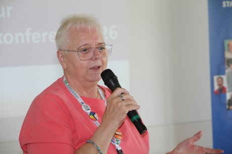 Frau in rosa T-Shirt ist aufgestanden, um sich per Mikro zu Wort zu melden. 
