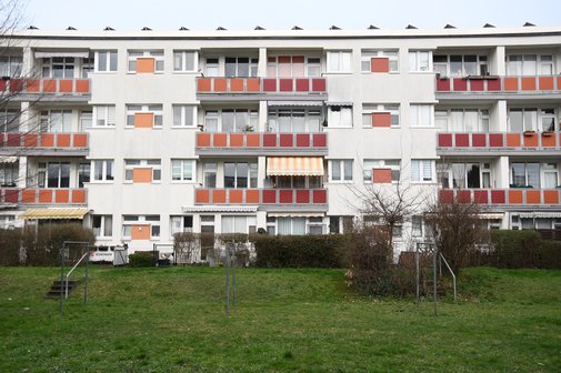 Blick auf einen Wohnblock mit etwa 20 Wohnungen. Im Vordergrund eine Gr&uuml;nanlage. 