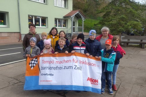 Kindergruppe steht zusammen hinter einem Transparent, das mehr Tempo bei der Verwirklichung von Inklusion fordert.