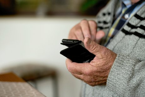 Älterer Mann in Strickjacke tippt auf seinem Handy