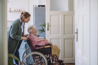 Eine jüngere Frau schiebt eine ältere Frau im Rollstuhl durch ihre Wohnung