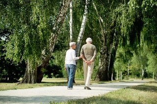 Man sieht zwei ältere Menschen, die in einem Park spazieren gehen.