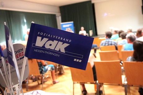 VdK-Papierf&auml;hnchen im Vordergrund, voll besetzte Sitzreihen im Hintergrund. 