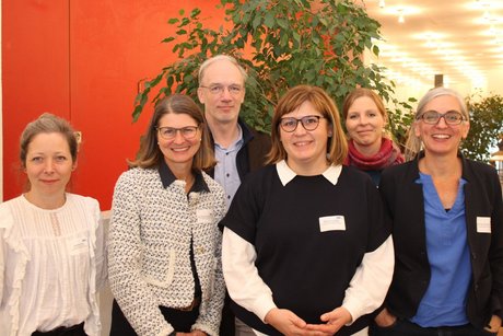 5 Frauen und ein Mann posieren vor einer leuchtend roten Wand.