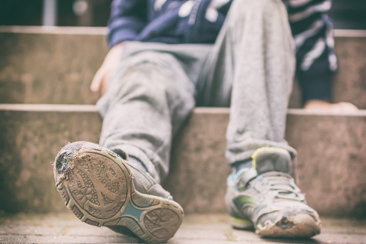 Junge sitzt auf einer Treppe, die Sohlen seiner Turnschuhe sind durchgelaufen.