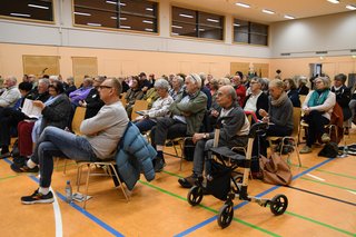 Etwa 40 Menschen auf Stühlen in einer Sporthalle 