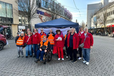 Große Frauengruppe in roten Jacken steht vor einem bkauben Zeltdach mit VdK-Transparent. 