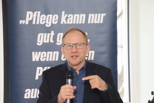 Mann steht vor Roll-up und erklärt Sachverhalt. 