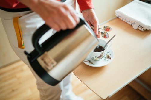 Eine Frau steht an einem Tisch und schenkt aus einer Thermoskanne Kaffee in eine Tasse ein. e