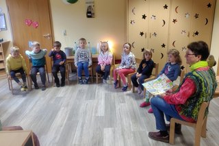 Kinder sitzen im Stuhlkreis und verfolgen aufmerksam die Geschichte von Käpt'n Kork, die ihnen von einer vdK-Ehrenamtlichen vorgelesen wird. 