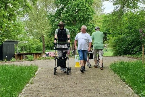 Zwei Männer mit Rollator und ein anderer Mann in einem Park