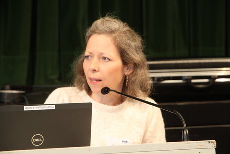 Referentin Katinka Götz Frau im weißen Shirt blickt zur Seite, während sie in ein Mikro spricht.