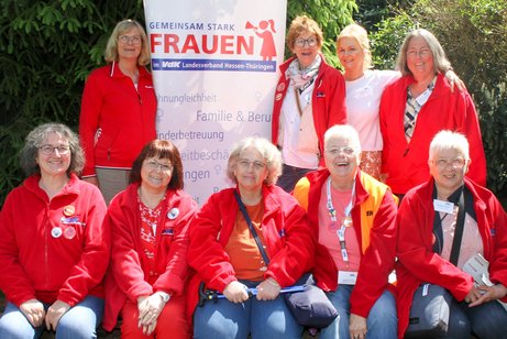 9 Frauen, eine in wei&szlig;er, alle anderen in roter Kleidung, haben sich vor einem Roll-up mit dem Emblem der VdK-Frauen gruppiert. 