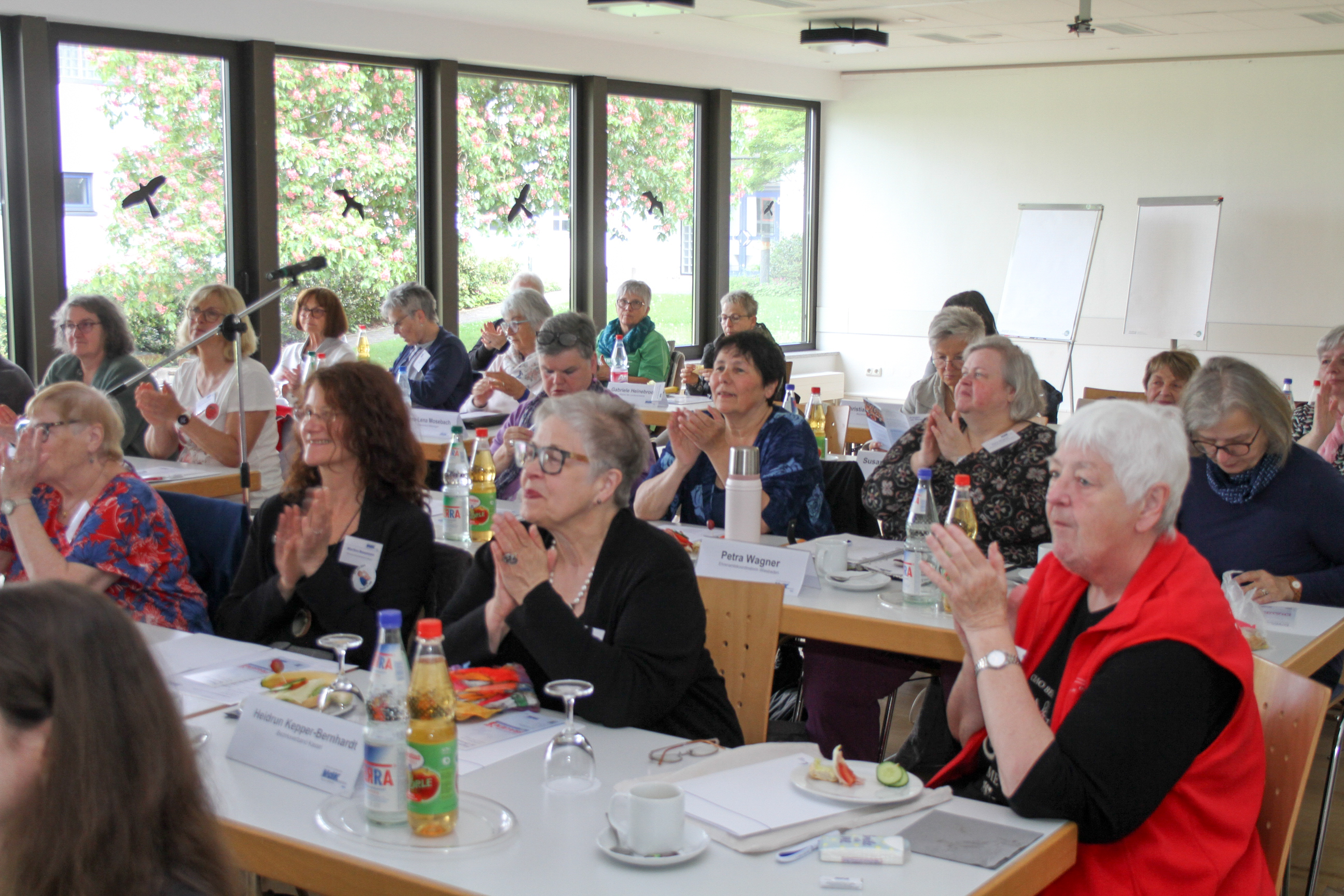 Seminarraum mit langen Tischreihen und gro&szlig;en Fenstern an der einen langen Seiten, gut gef&uuml;llt, mit vielen Frauen, die interessiert zuh&ouml;ren. 