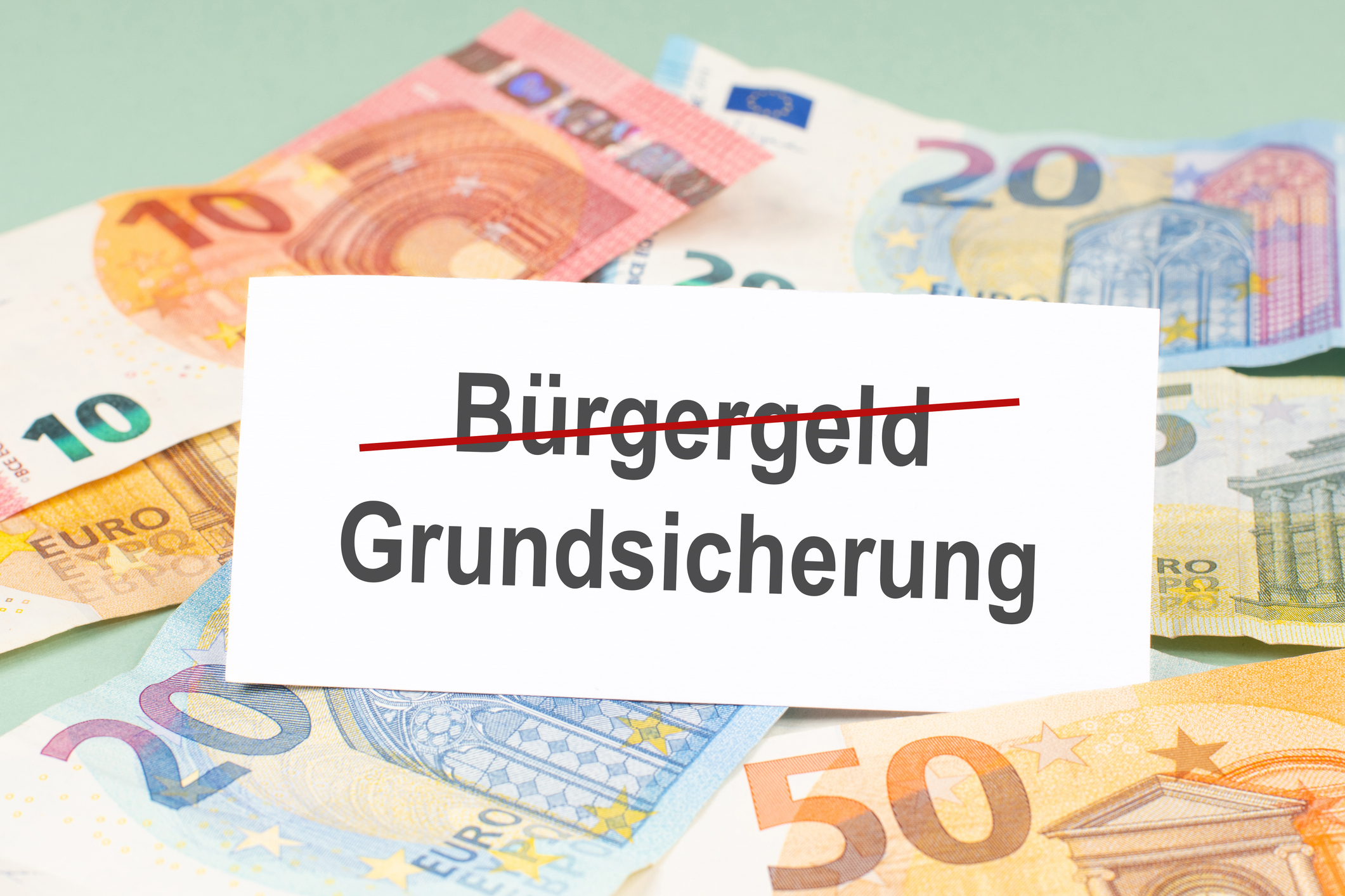 Neue Grundsicherung löst Bürgergeld ab 10-, 20- und 50-Euro-Geldscheine vor hellgrünem Hintergrund mit weißer Fläche, auf der die Wörter Bürgergeld und Grundsicherung stehen