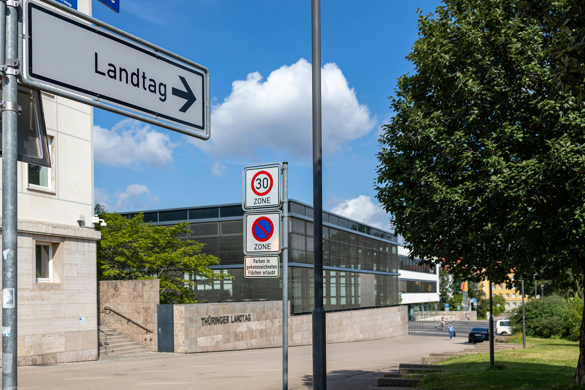 Thüringer Landtag: Ein Schild mit der Beschriftung Landtag und dem Straßennamen Jürgen-Fuchs-Straße ist im Vordergrund zu sehen, während im Hintergrund das Gebäude des Plenarsaals des Thüringer Landtags in Erfurt zu sehen ist.