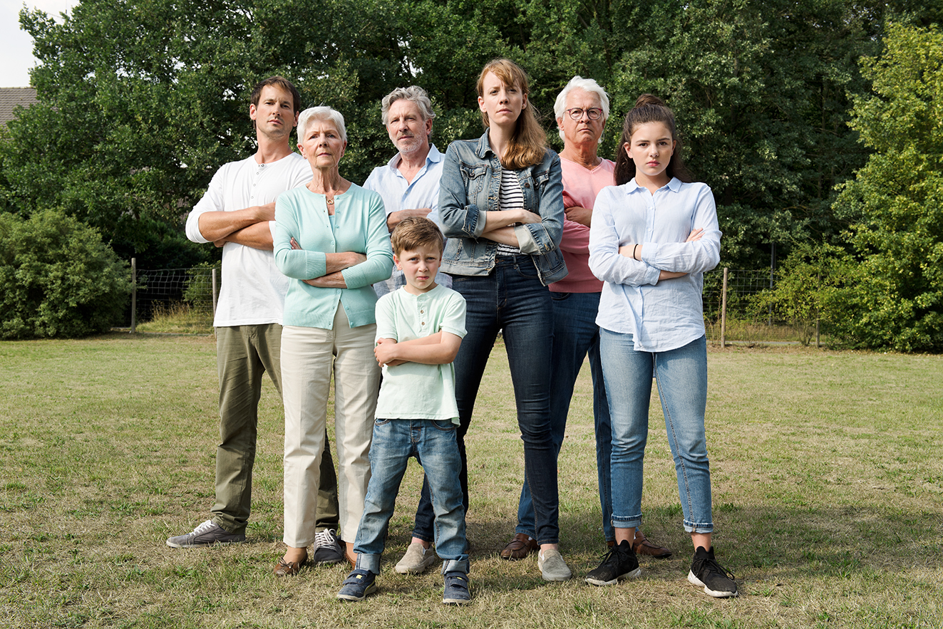 Eine Gruppe von Erwachsenen und Kindern steht als Gruppe dicht beeinander, sie blicken ernst, haben die Arme ablehnend verschr&auml;nkt. 