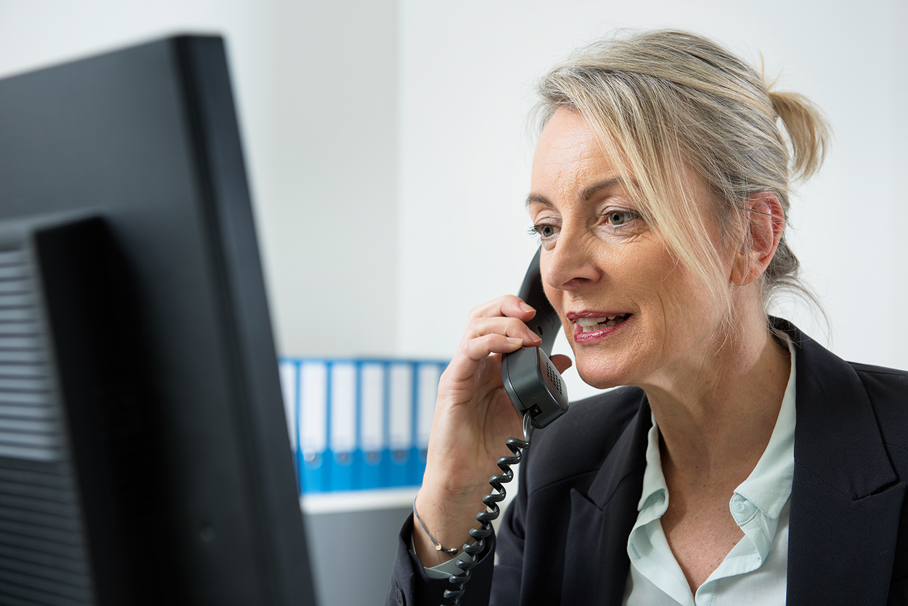 VdK-Beratung Eine Frau am Computer, sie telefoniert. Im Hintergrund sieht man Aktenordner.
