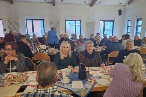 Ein Saal mit mehreren Tischen an denen eine Vielzahl von meist &auml;lteren Menschen sitzen, sie haben Kaffee und Stollen auf den weihnachtlich eingedeckten Tischen stehen.