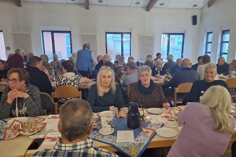Ein Saal mit mehreren Tischen an denen eine Vielzahl von meist &auml;lteren Menschen sitzen, sie haben Kaffee und Stollen auf den weihnachtlich eingedeckten Tischen stehen.