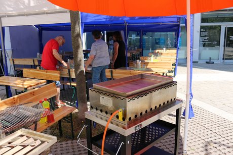 Der Gasgrill wird aufgebaut, im Hintergrund Mitglieder des Orga-Teams bei den Vorbereitungen