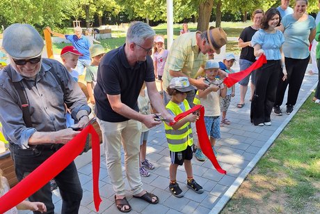 Der Park wird nach seiner Neugestaltung freigegeben. Der Bürgermeister (Bildmitte) wird dabei tatkräftig durch anwesende Kinder unterstützt.