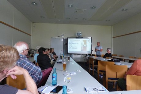 man sieht verschiedene personen an tischen sitzen und zur computerleinwand schauen